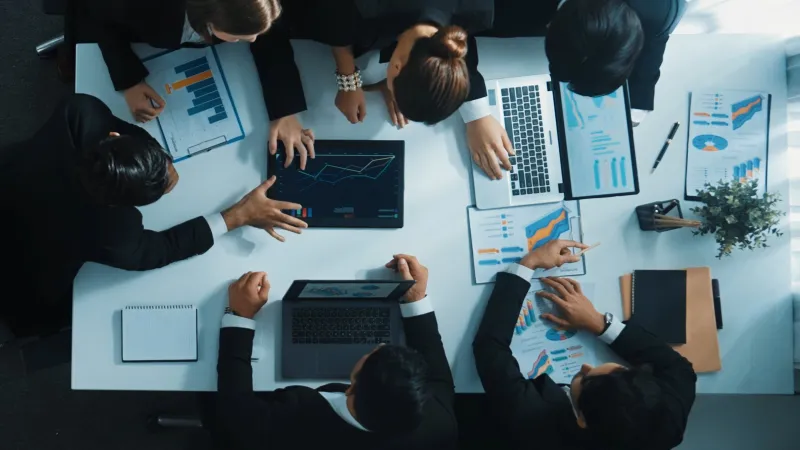 Business team collaborating on financial charts and data analysis around a table with laptops and documents.