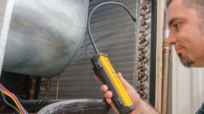 Technician inspecting HVAC system using a handheld diagnostic tool near copper coils and wiring.