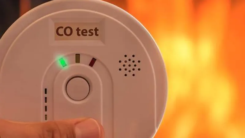 Hand holding a CO test detector with green light indicating safety against a fiery orange background.