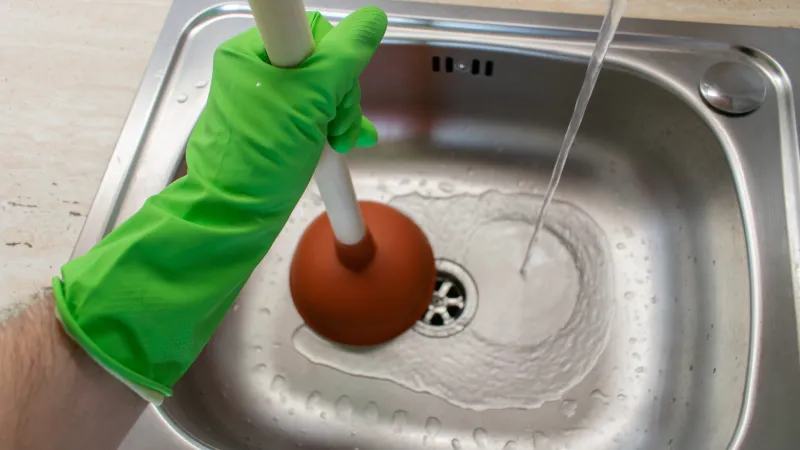 a hand holding a green object above a metal sink with a round object