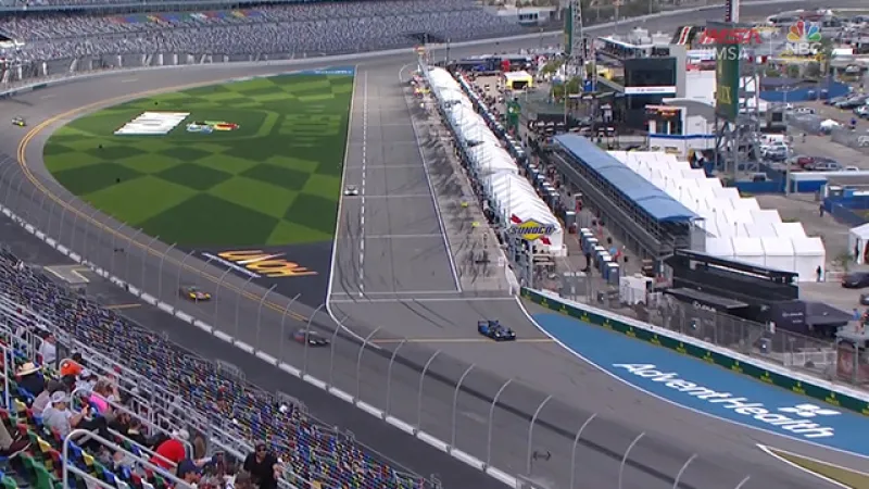 Aerial view of a race track with cars on the circuit and spectators in the grandstands during a motorsport event.