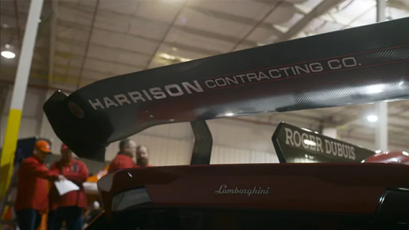 Close-up of Lamborghini race car rear wing with Harrison Contracting and Roger Dubuis branding indoors