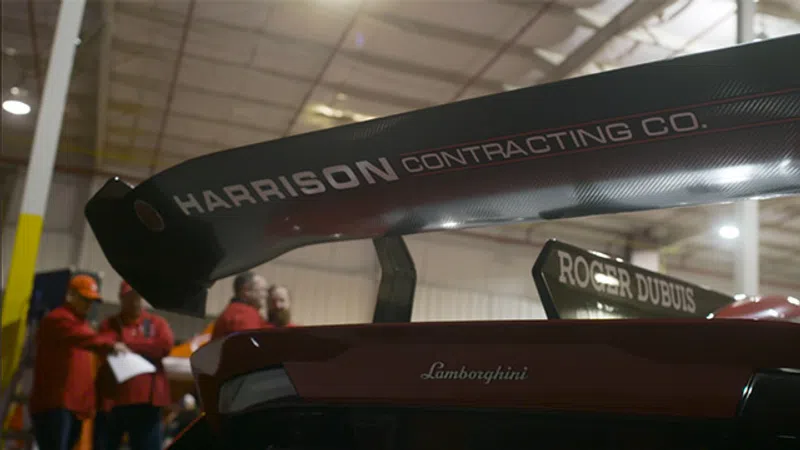 Close-up of Lamborghini race car rear wing with Harrison Contracting and Roger Dubuis branding indoors