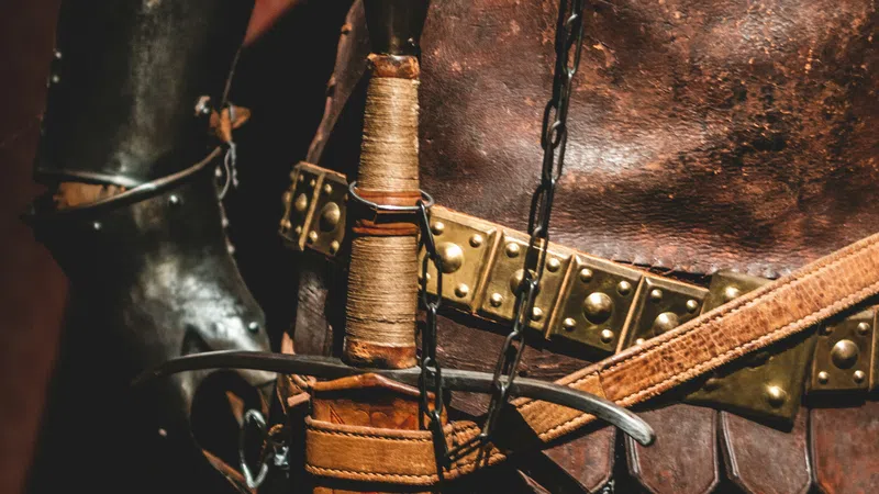 Close-up of medieval armor details including chainmail, leather belt, and sword hilt with wrapped handle.