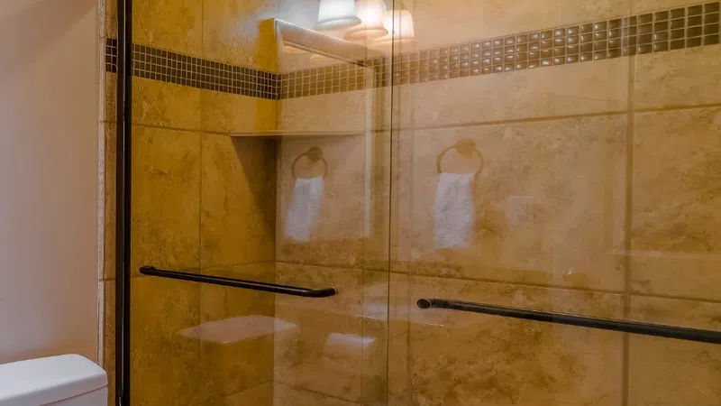 Modern bathroom with beige tiled walk-in shower featuring glass doors and a white toilet beside it.