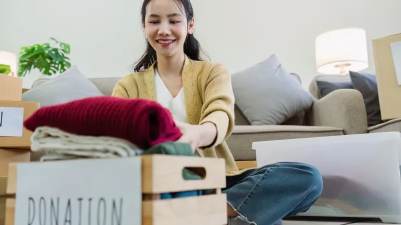 Woman organizing donations in a cozy living room, folding clothes into a donation box.