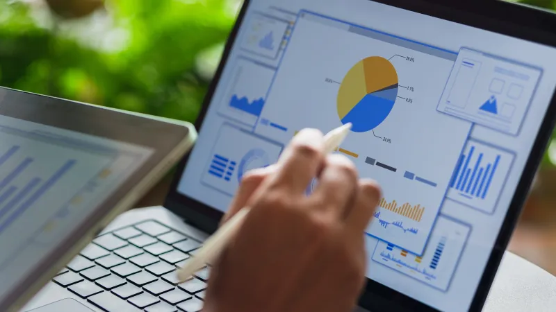 Person using stylus to interact with charts and graphs on a laptop screen showing data analysis.