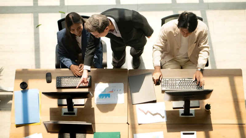 Business team collaborating at office desks with computers and charts in natural light from above