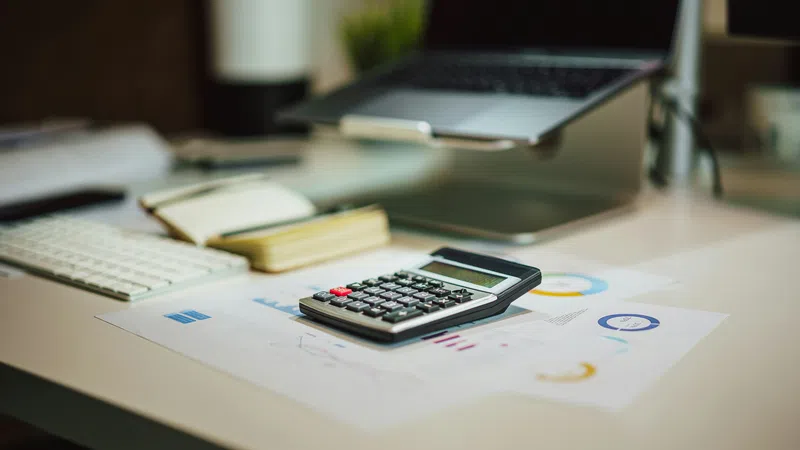 Calculator on printed charts with laptop, keyboard, and notebook on a clean office desk workspace.