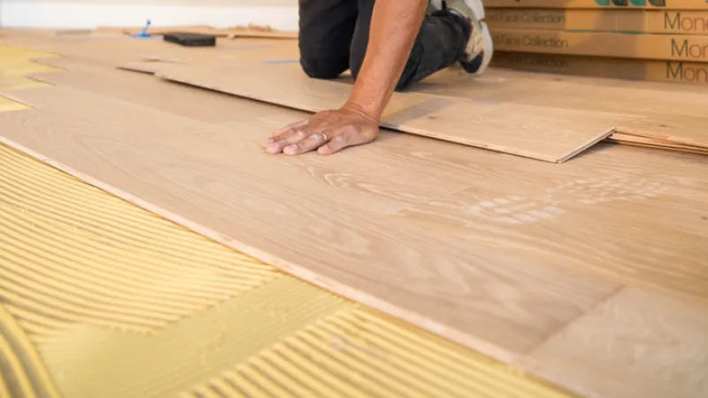 Worker using rubber mallet to install wooden flooring while kneeling in a residential interior space.