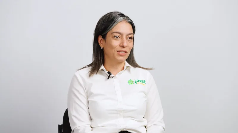 Woman in white Pest Control branded shirt speaking in an interview against a plain background.