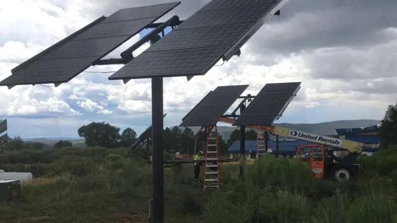 Solar panel array installation in a field under cloudy sky with construction equipment and workers nearby