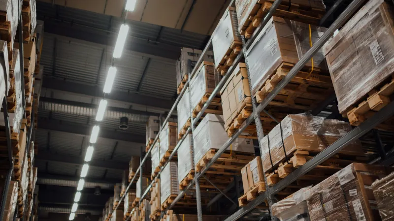 Warehouse shelves stacked with pallets of boxed goods under bright industrial lighting.
