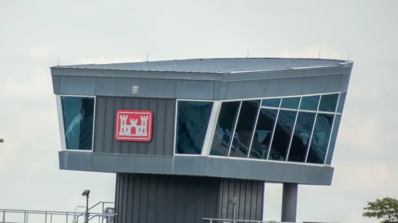Modern gray control tower with large angled windows and a red castle emblem on the side under cloudy sky