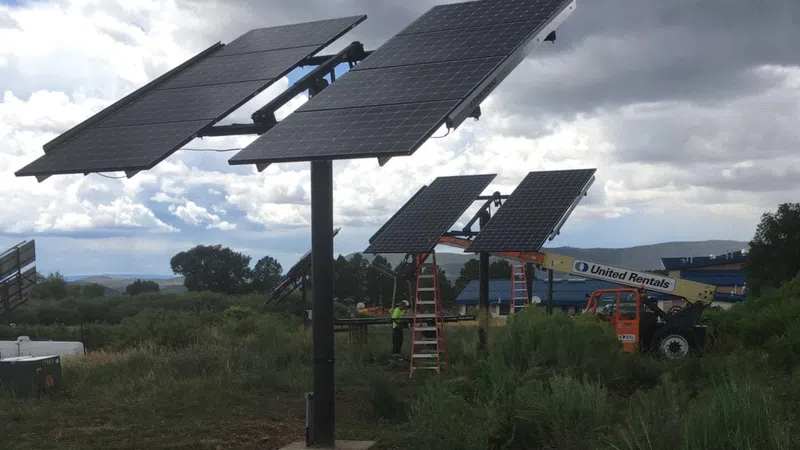 Solar panels mounted on poles in a field with workers and equipment under a cloudy sky.
