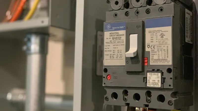 Close-up of an industrial circuit breaker panel with wires and labels inside an electrical box.