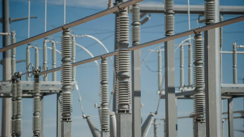 Close-up of electrical substation insulators and metal structures against a clear blue sky background.