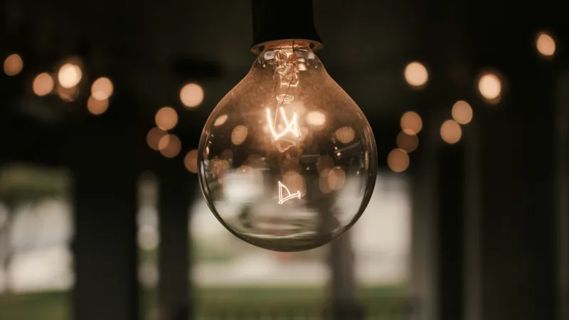 Close-up of a glowing vintage light bulb with blurred warm fairy lights in the background.