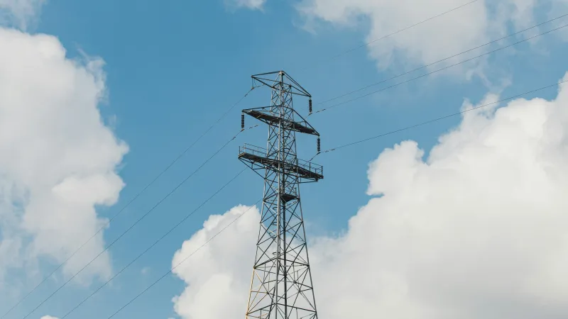 High voltage power transmission tower against blue sky with white clouds on a sunny day