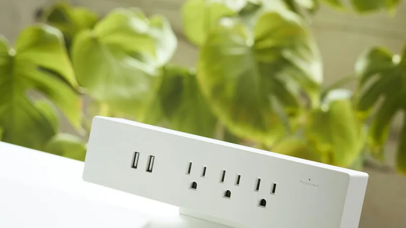 White power strip with USB ports and outlets mounted on a white desk with green plants in the background