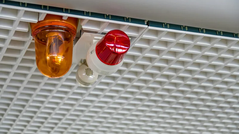 Red and orange emergency warning lights mounted on a white grid ceiling in an industrial setting.