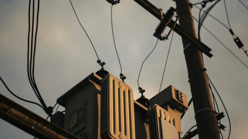 Electric transformer mounted on wooden utility pole with wires against cloudy sky at dusk.