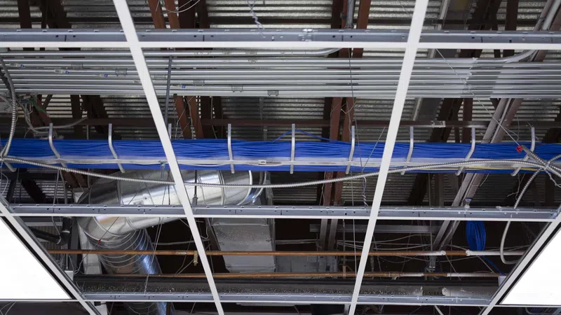Exposed ceiling grid with HVAC ducts and blue electrical cables in a commercial building under renovation.