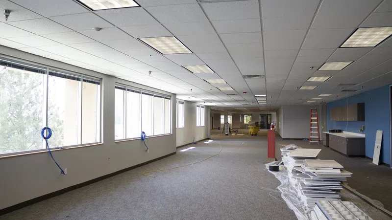 Spacious office interior under renovation with carpet flooring, ceiling lights, and construction materials.