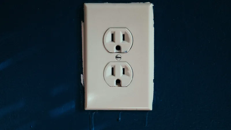 White electrical outlet on dark blue wall with shadows and slight paint drips below it
