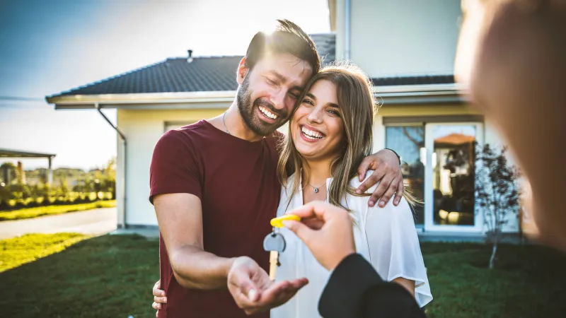 Happy couple receiving house keys from a real estate agent in front of their new home on a sunny day