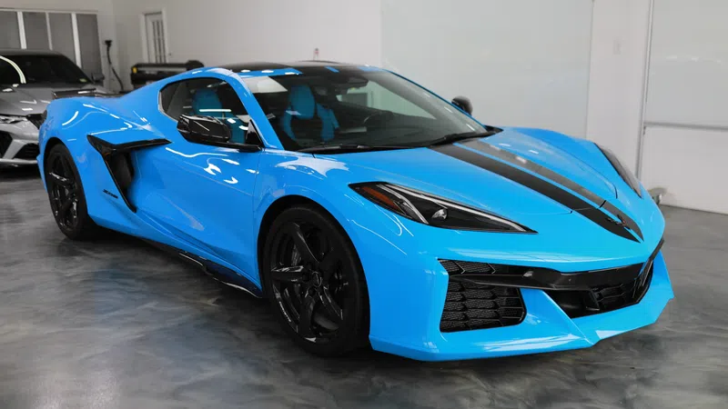 Blue sports car with black racing stripe parked indoors on polished concrete floor.