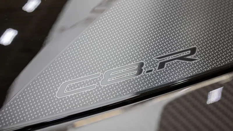 Close-up of Corvette C8.R logo on textured carbon fiber car part with reflective surfaces and lighting.