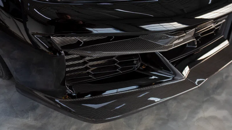 Close-up of a sleek black car's front bumper featuring carbon fiber accents and modern grille design.