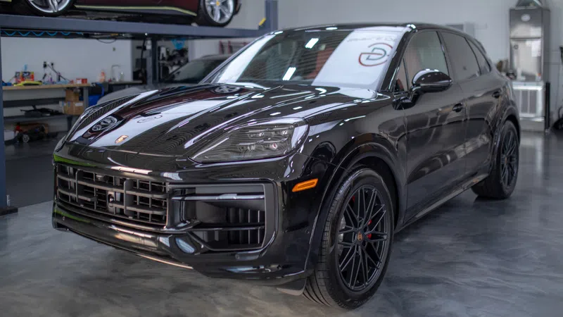 Black luxury Porsche SUV parked inside a modern garage with polished concrete floor and another car on a lift.