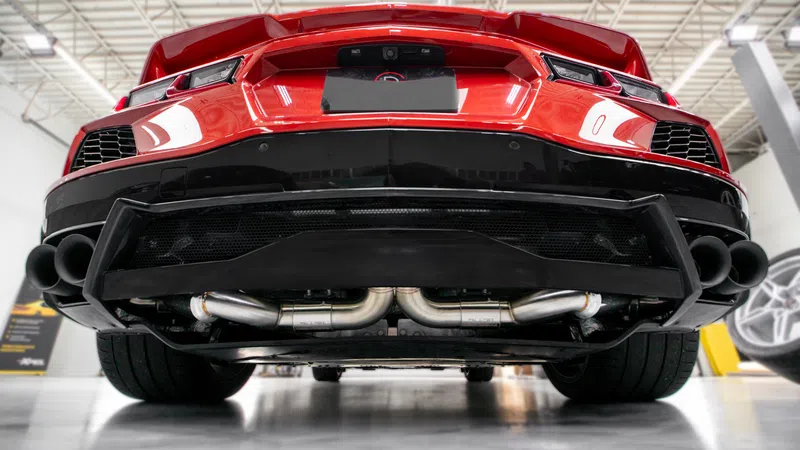 Low angle view of a red sports car rear showcasing exhaust pipes and diffuser under bright garage lighting