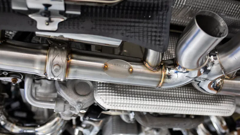 Close-up of stainless steel aftermarket car exhaust system showing pipes and welds under vehicle.