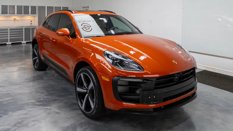 Orange Porsche SUV parked in a modern showroom with polished concrete floor and white walls.