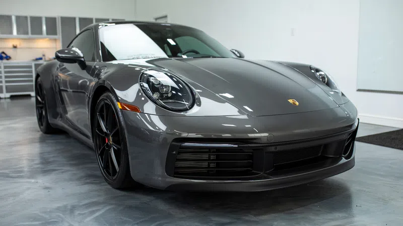 Sleek gray Porsche 911 sports car parked indoors on polished concrete floor with black wheels and modern headlights.