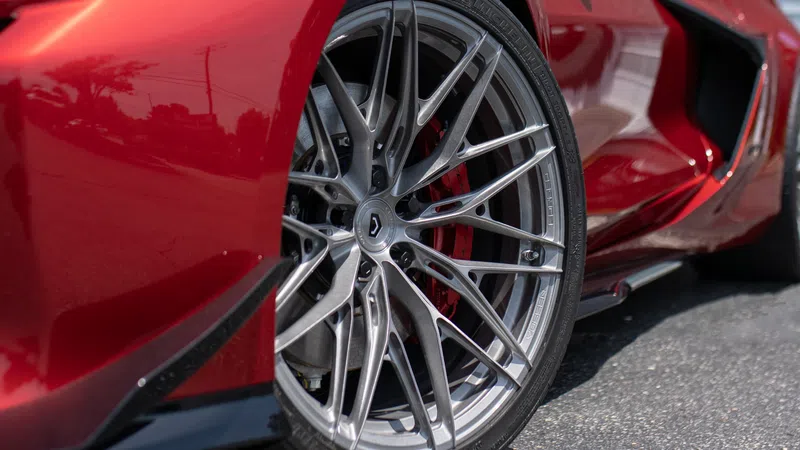 Close-up of sleek silver alloy wheel on red sports car with detailed tire and brake components.