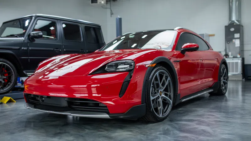 Red Porsche Taycan electric sports car parked indoors beside a black SUV on polished floor.