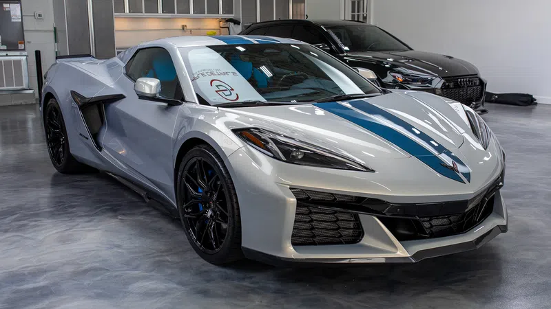 Silver sports car with blue racing stripe parked in a polished showroom with another black car in background