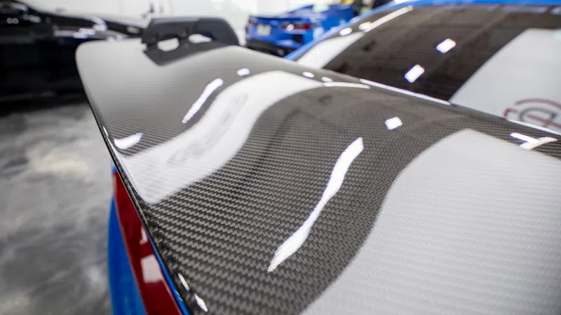 Close-up of a glossy carbon fiber car spoiler with reflections in a garage setting