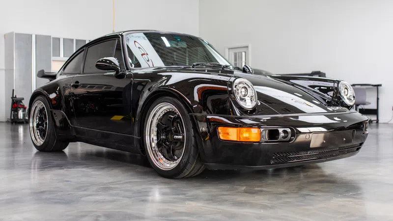 Black vintage Porsche sports car with wide body kit parked indoors on polished concrete floor.