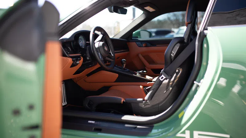 Interior view of a green sports car showing black and tan leather seats, steering wheel, and dashboard.