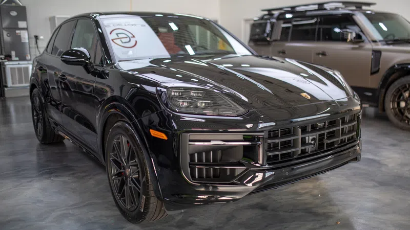 Black luxury Porsche SUV parked indoors with sleek design and modern headlight features.