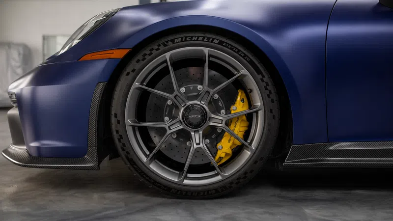 Close-up of matte blue sports car front wheel with yellow brake caliper and Michelin tire in garage