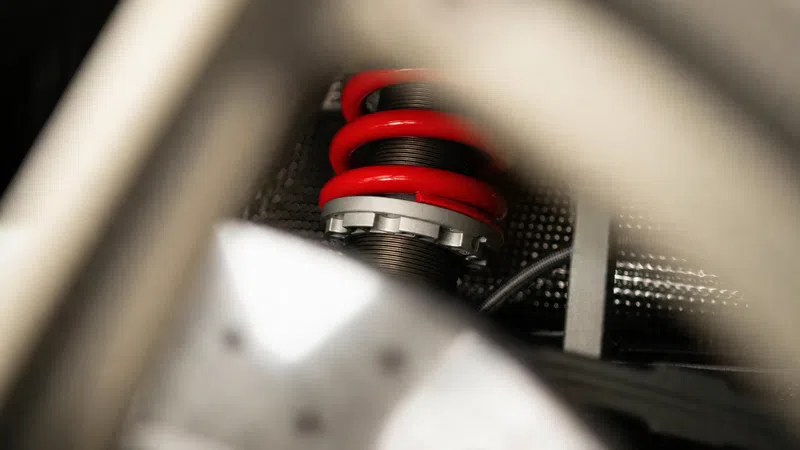 Close-up of a red coil spring on a shock absorber inside a vehicle suspension system.