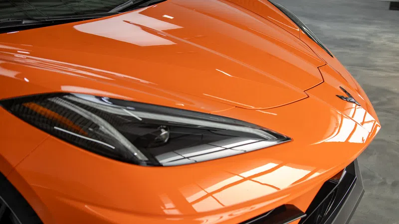 Close-up of the front end of an orange sports car highlighting its sleek headlight and hood design.