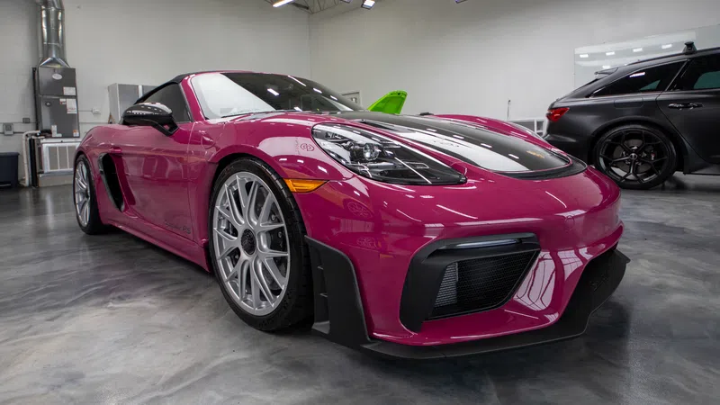Sleek magenta sports car with silver rims parked inside a glossy showroom with other vehicles.