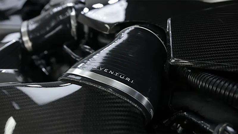 Close-up of a black carbon fiber engine component with a metal clamp and Venturi branding.
